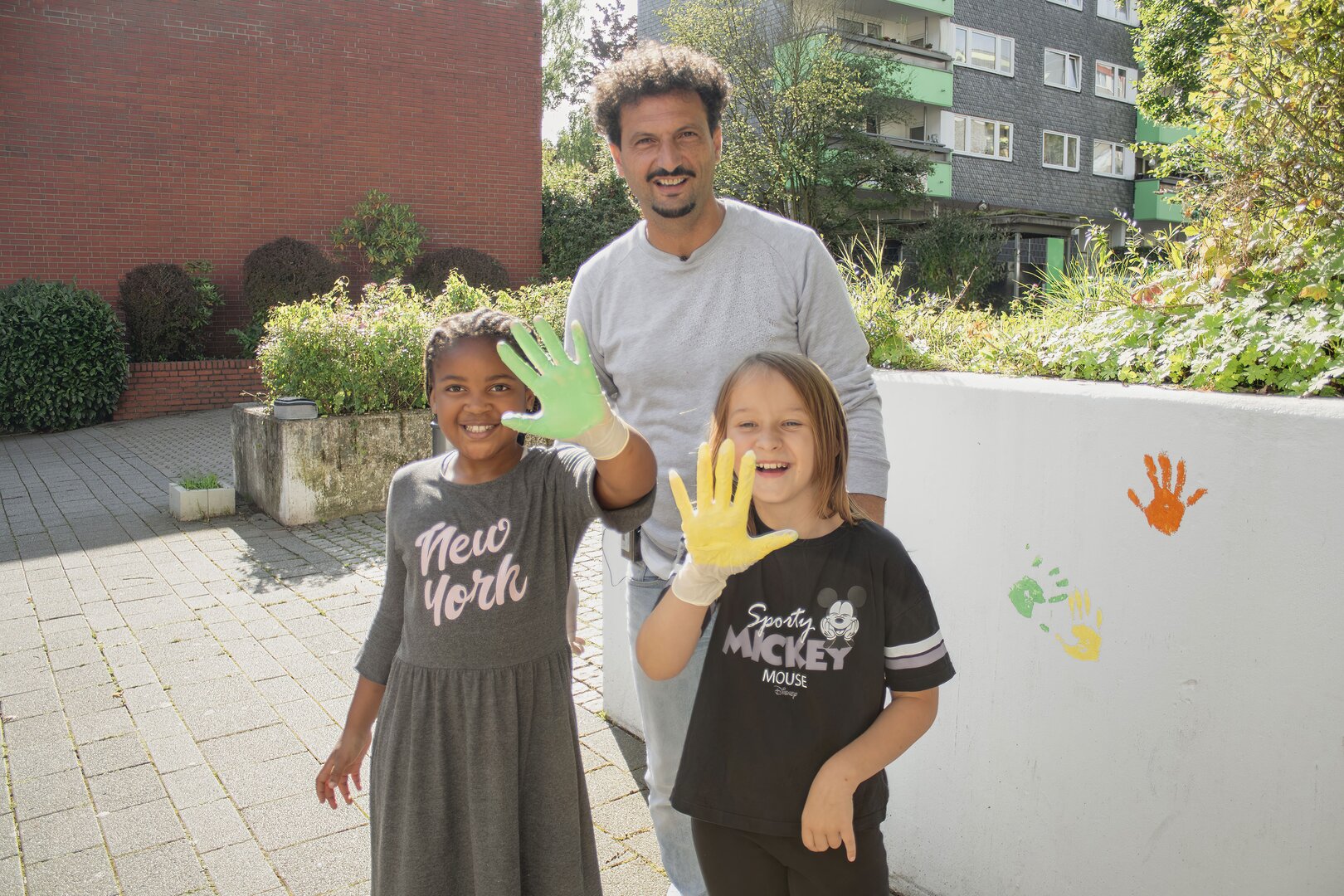 Quartiersexperte Faruk Yildirim zusammen mit zwei Kindern, die bereit für ihre beiden Handabdrücke an der ehemaligen Graffiti-Mauer sind