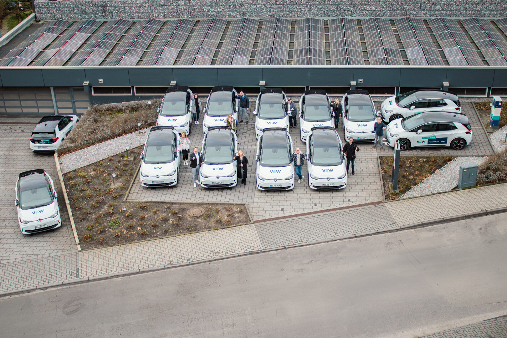 VBW-Mitarbeitende freuen sich über die neue E-Fahrzeugflotte, die neben der E-Ladesäule und der Photovoltaik-Anlage steht.